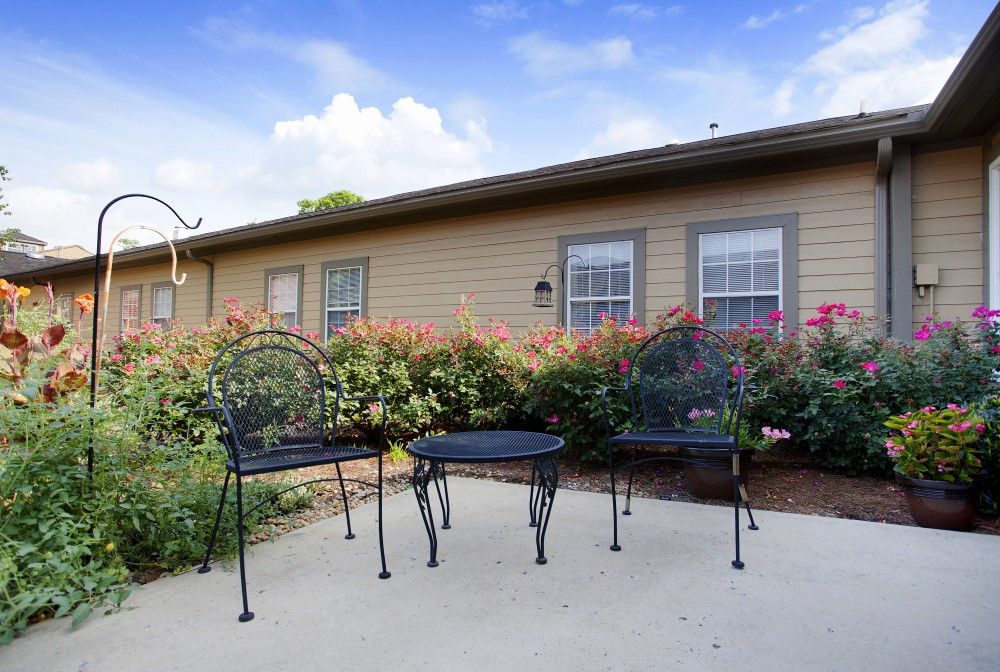 A cozy patio set with two chairs and a table surrounded by vibrant flowers in an outdoor garden setting.