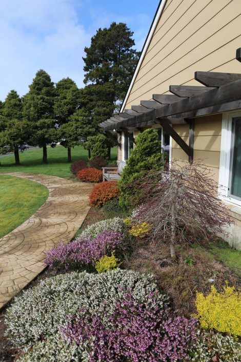 A well-maintained garden with colorful plants and a stone sidewalk beside a house.