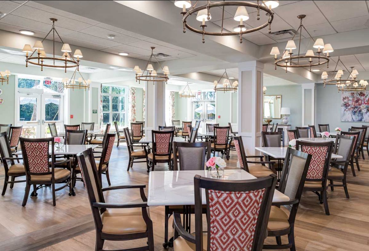 An elegant dining room with neatly arranged tables and chairs, illuminated by chandeliers.