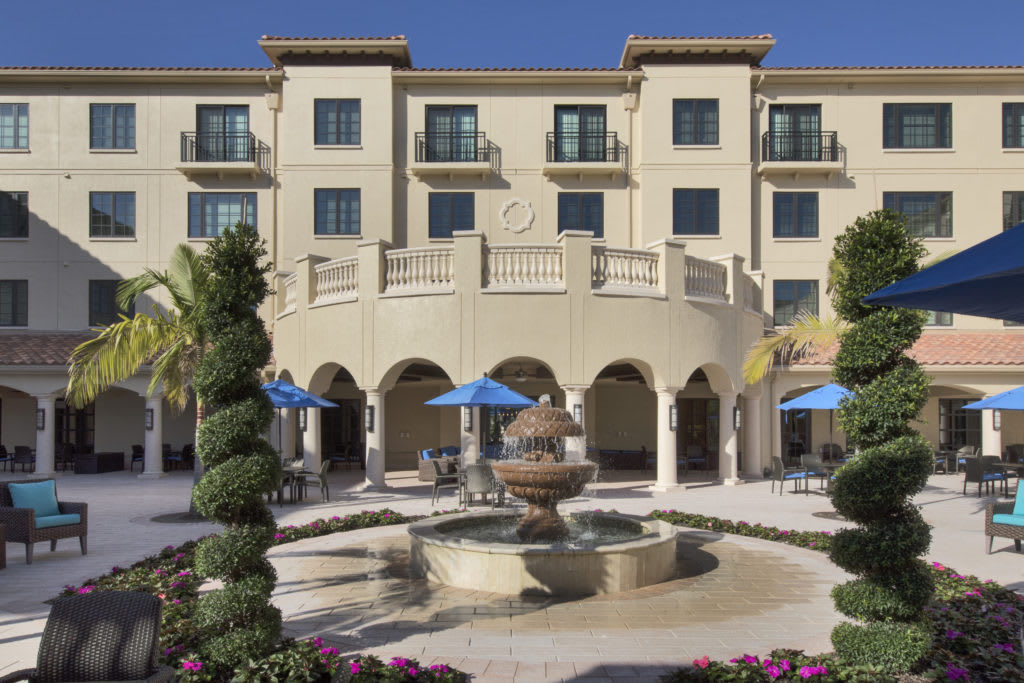 A view of a hotel courtyard featuring a central fountain and outdoor seating with blue umbrellas.