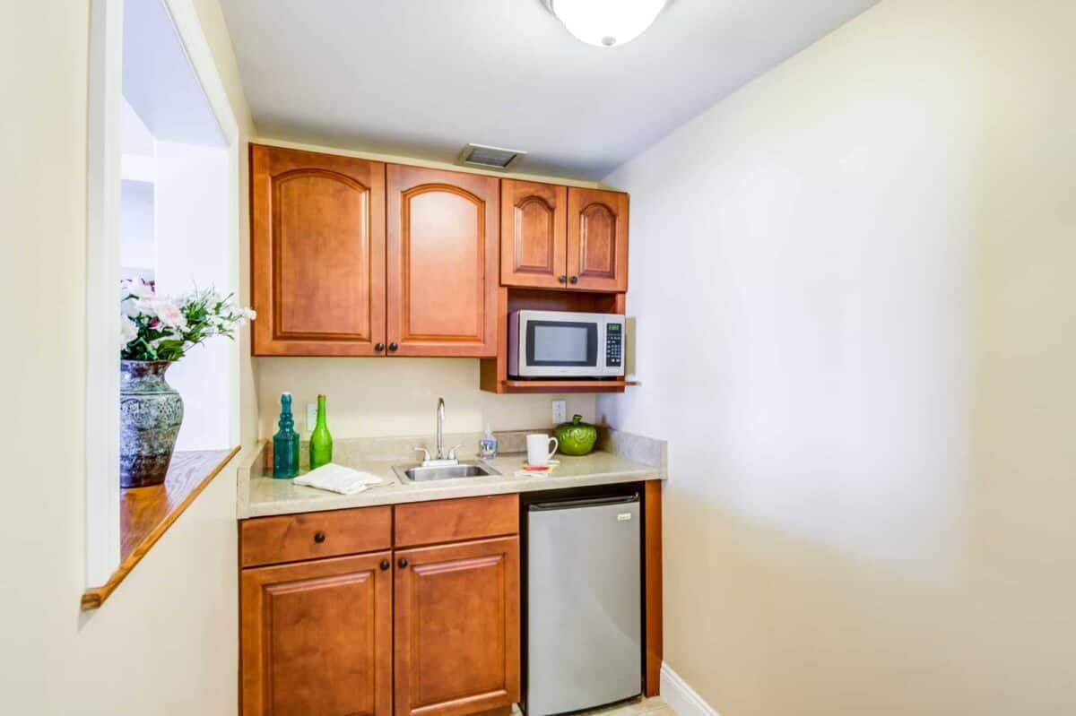 A compact kitchenette with wooden cabinets, a microwave, mini fridge, and sink.