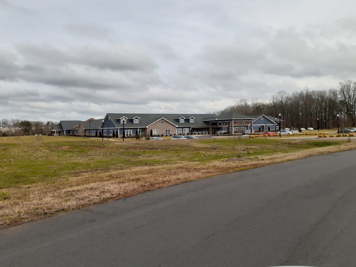 A large building under construction on a cloudy day with an adjacent road and open grassy area.