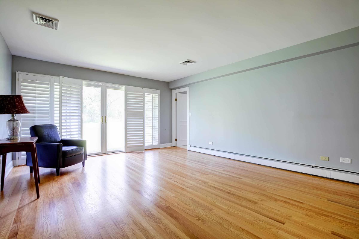 A spacious, sunlit room with hardwood flooring and large windows.