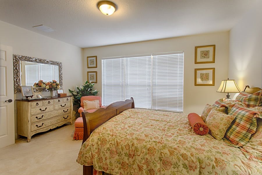 A cozy bedroom with a floral-patterned bed, a dresser, and large window blinds.