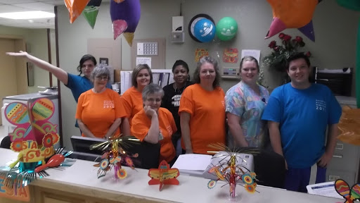 A group of staff members in orange shirts gathered at the office for a celebration.