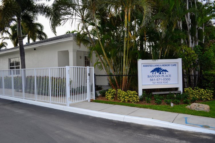 Entrance to a building with a gate and sign surrounded by palm trees.