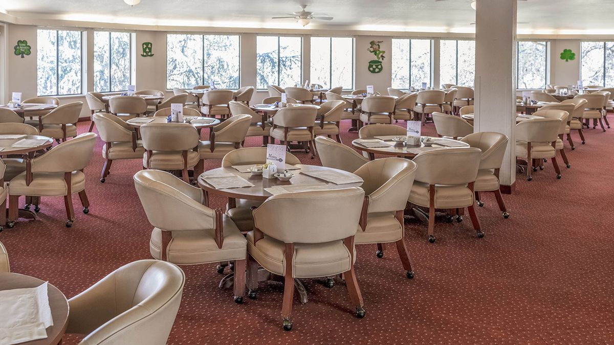 An empty dining room with neatly arranged chairs and tables on a carpeted floor.