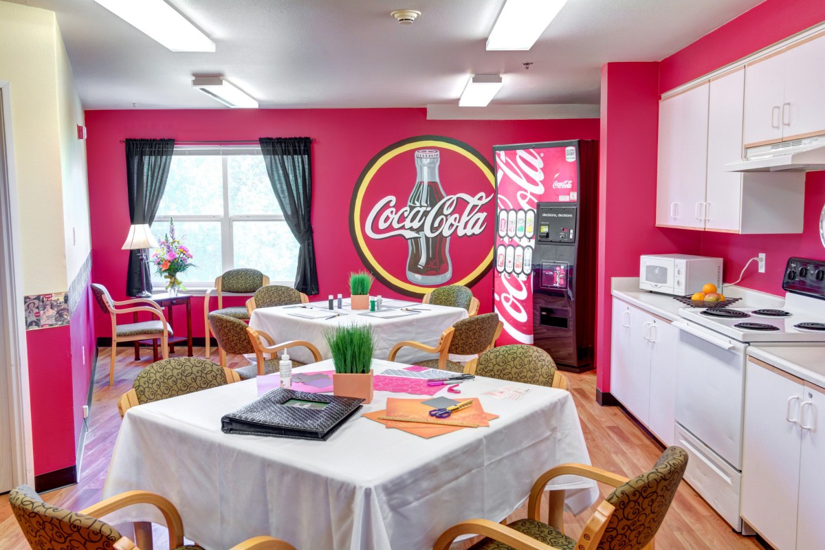 A vibrant dining area featuring a Coca-Cola themed decor with tables, chairs, and a vending machine.