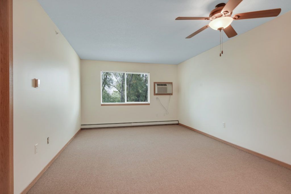 An empty room with carpet flooring, a window, ceiling fan, and wall-mounted air conditioner.