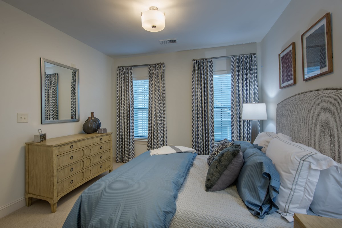 A modern bedroom with a neatly made bed, stylish curtains, and elegant lighting.
