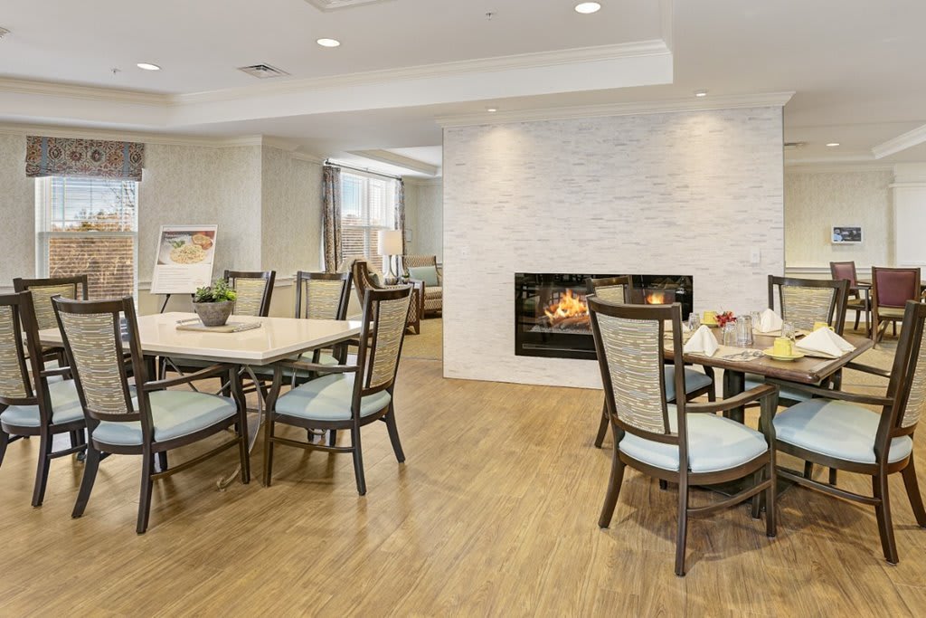 A modern dining area featuring elegant tables and chairs, with a cozy fireplace set into a white brick wall.