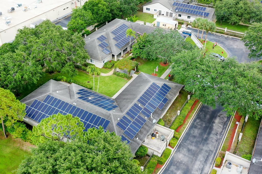 Aerial view of residential houses equipped with solar panels surrounded by lush greenery.