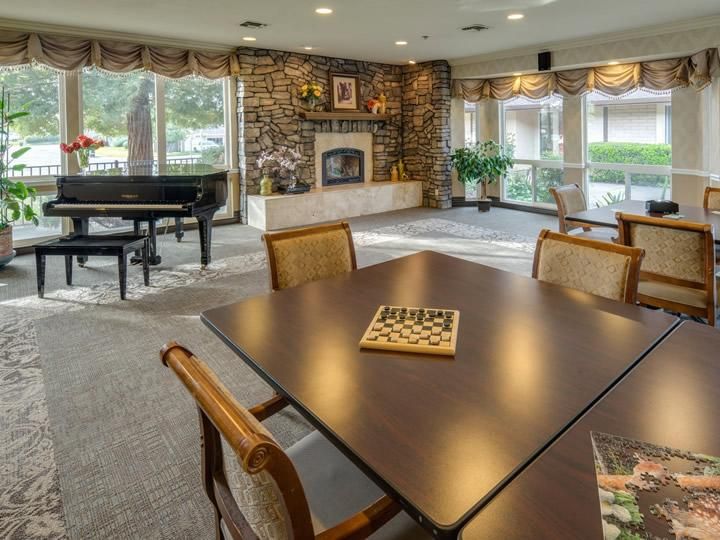 A cozy living room with a fireplace and piano, featuring a table set for board games.