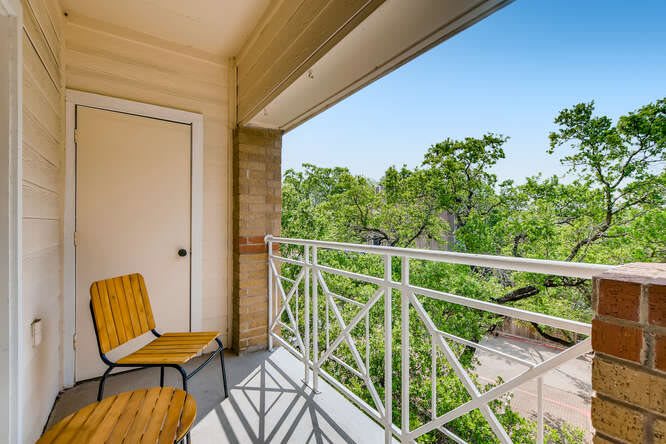 A peaceful balcony with seating and a view of lush green trees.