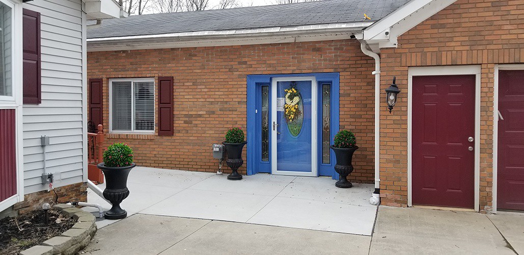 The front entrance of a brick building features a vibrant blue door with a decorative wreath and two black planters on either side.