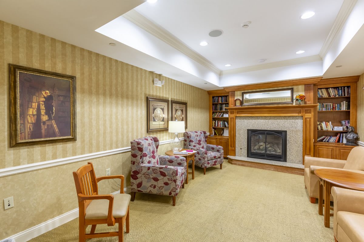 A cozy living room with patterned armchairs, a wooden bookshelf, and a fireplace.