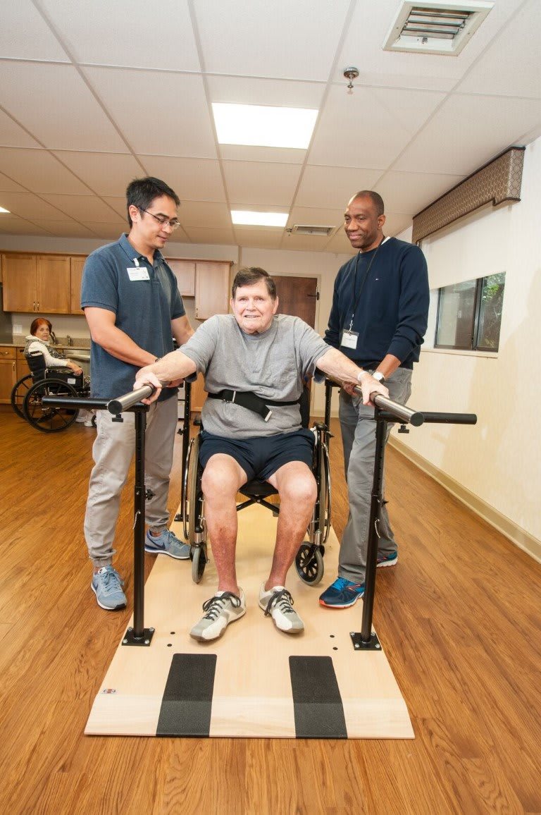 A person receiving support during a physical therapy session with two therapists assisting.
