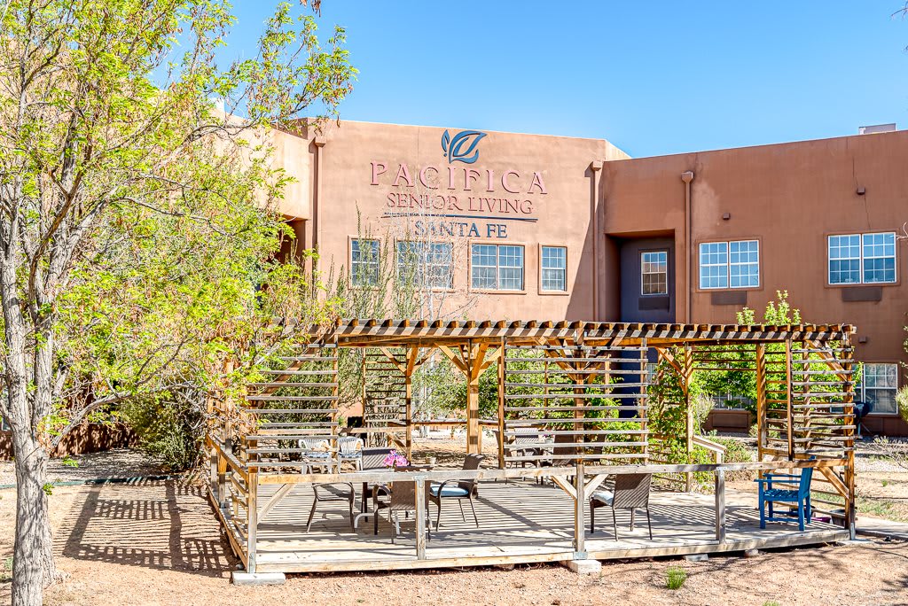 A view of a building with outdoor seating and pergola on a sunny day.