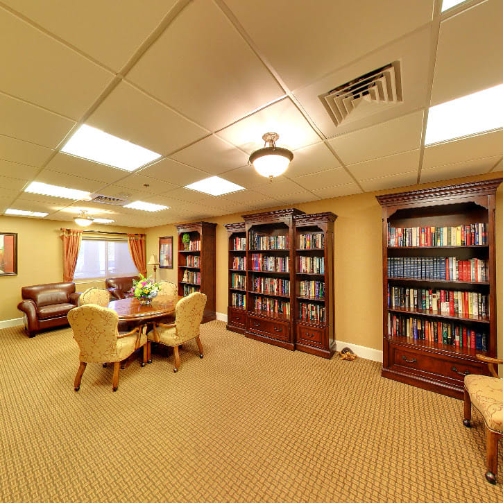 A cozy library room with wooden bookshelves filled with books, a conference table, and comfortable seating.