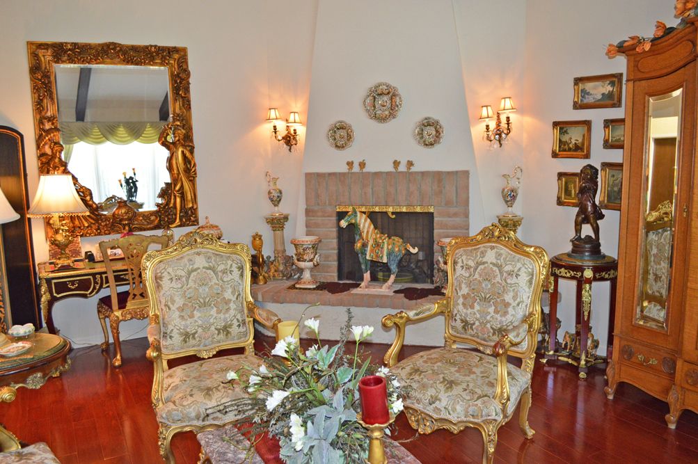 A classic living room with ornate furniture and a fireplace, featuring decorative mirrors and elegant armchairs.