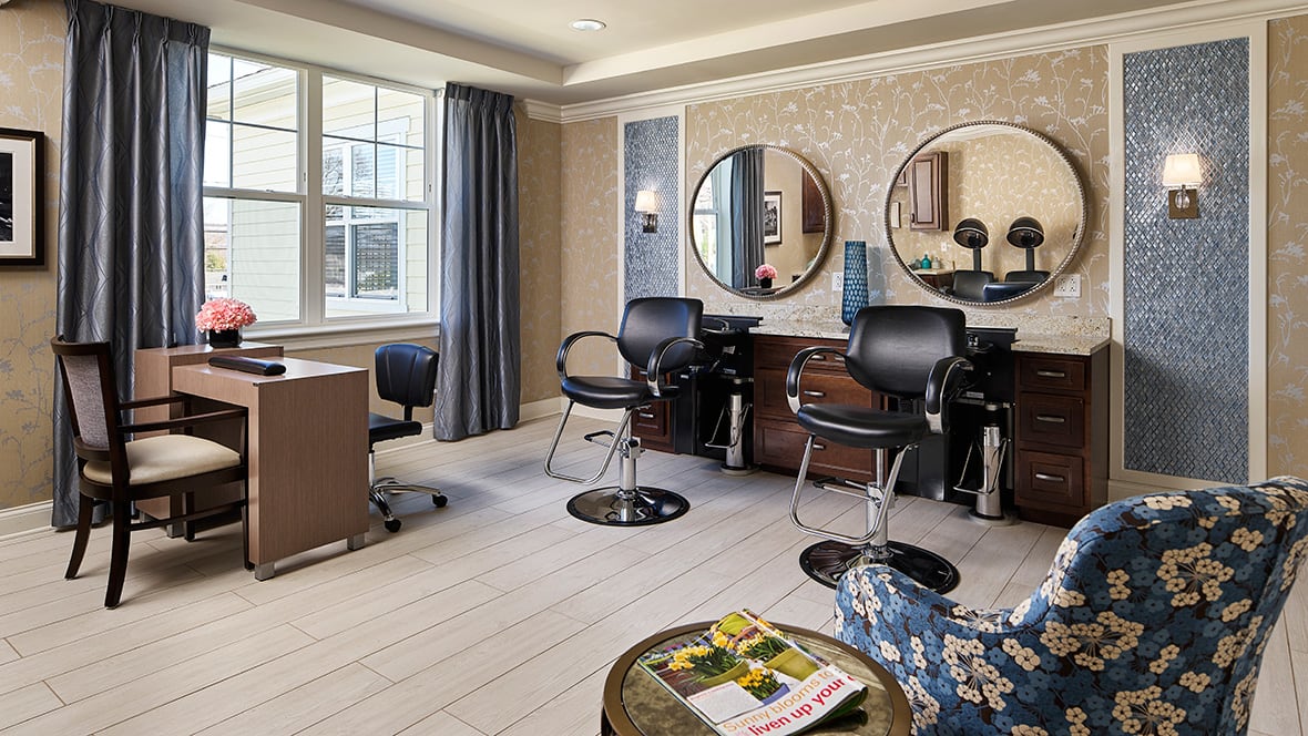 A well-lit salon interior with styling chairs, mirrors, and a desk near large windows.
