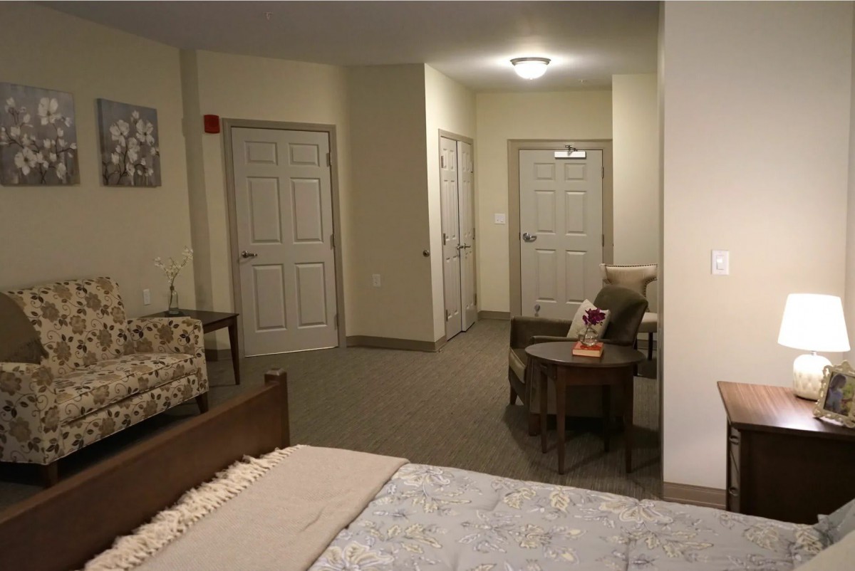 A cozy bedroom featuring a bed, chair, and small table, with multiple doors leading out of the room.