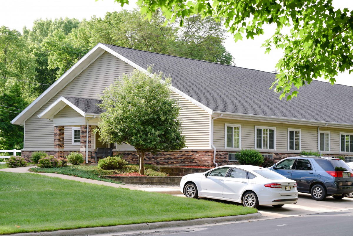 A suburban house with a well-maintained lawn and parked cars in the driveway.