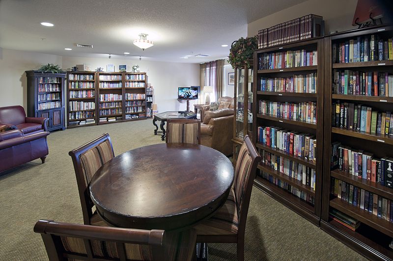 A cozy library reading area with bookshelves, tables, and chairs.