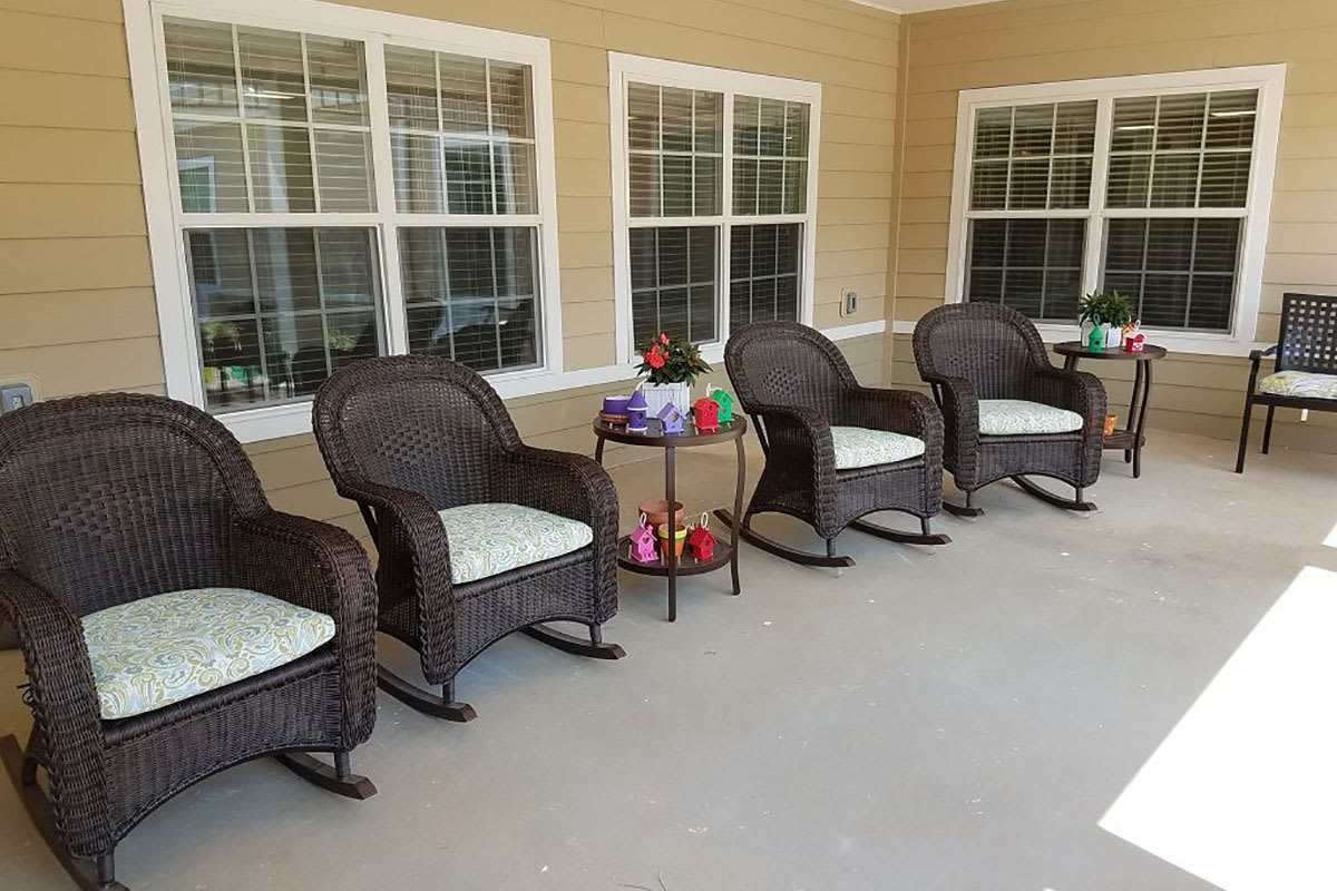 A cozy patio with wicker rocking chairs arranged in a row, accompanied by a small table and decorative items.