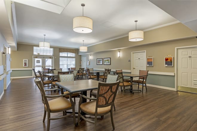A spacious dining room with wooden tables and chairs, well-lit by modern pendant lights.