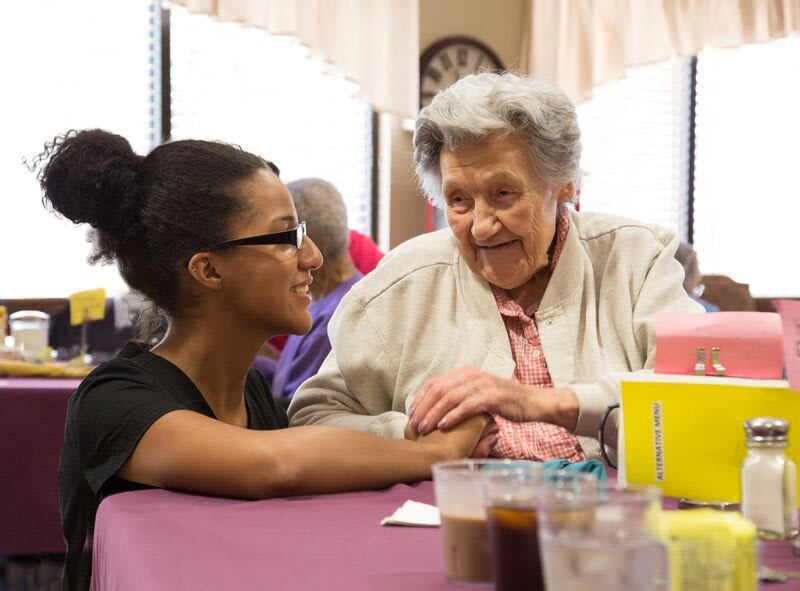 A young woman holds the hand of an elderly woman in a warm and caring interaction.