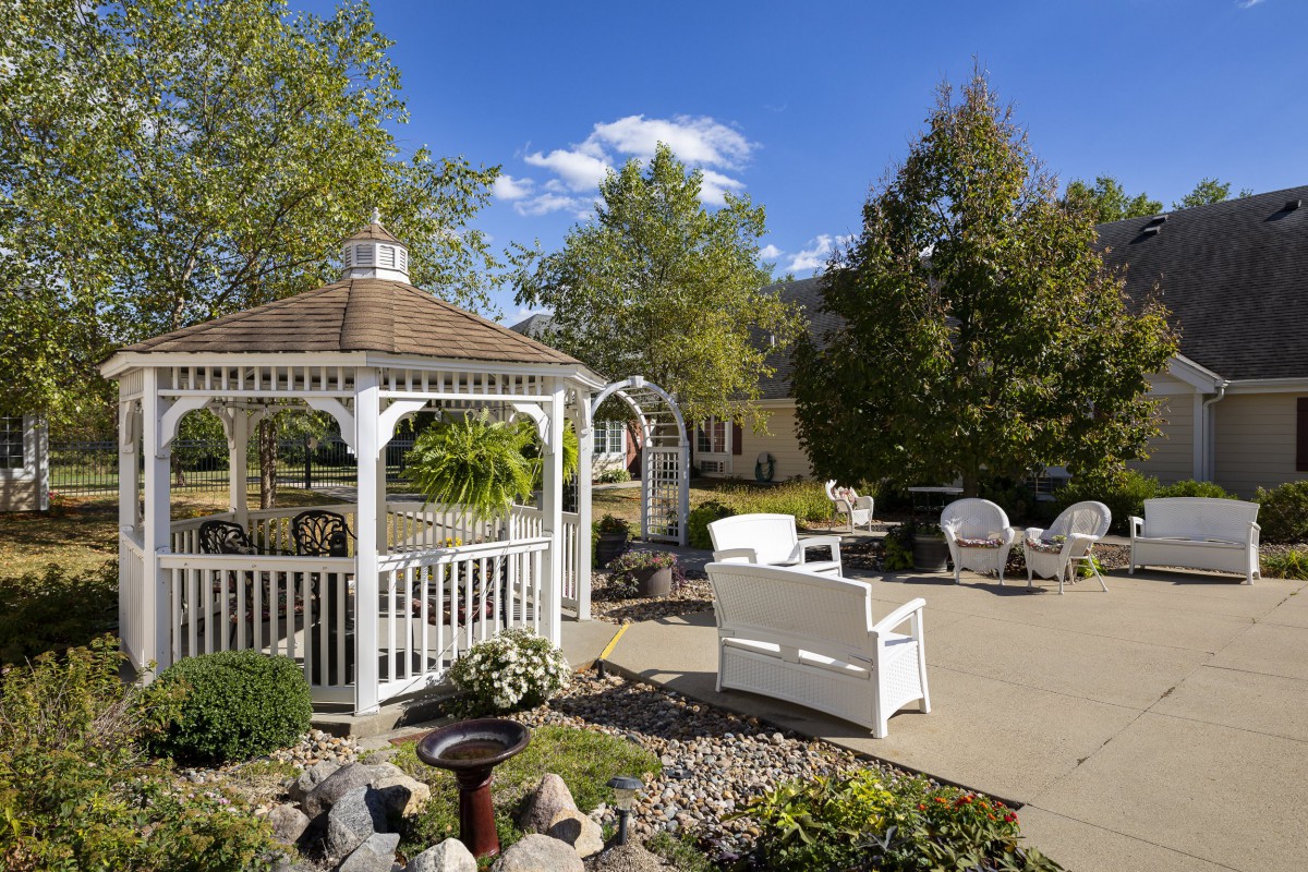 A peaceful garden setting with a white gazebo and outdoor seating on a sunny day.