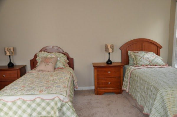 A cozy bedroom featuring two twin beds with a nightstand and lamp in between.