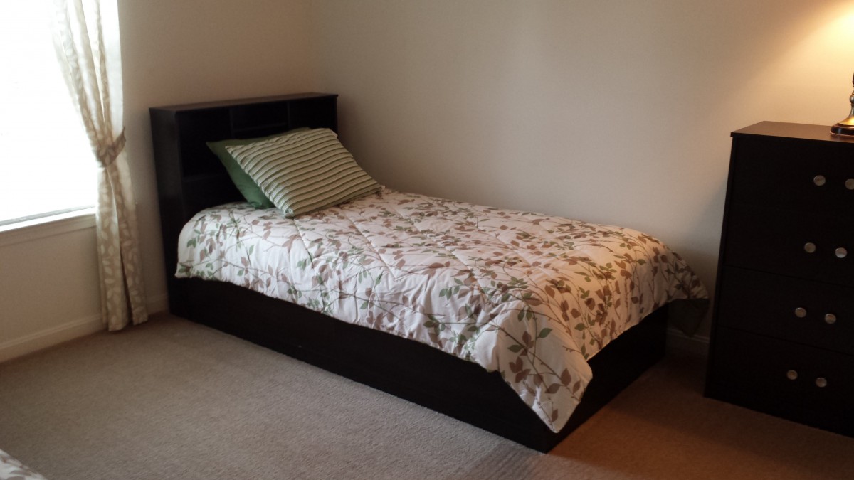 A neatly made single bed with a floral blanket and a striped pillow in a simple bedroom setting.