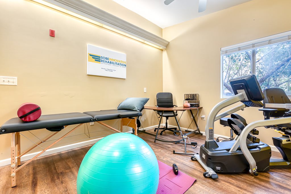 A fitness therapy room equipped with an exercise ball, stationary bike, and treatment table.