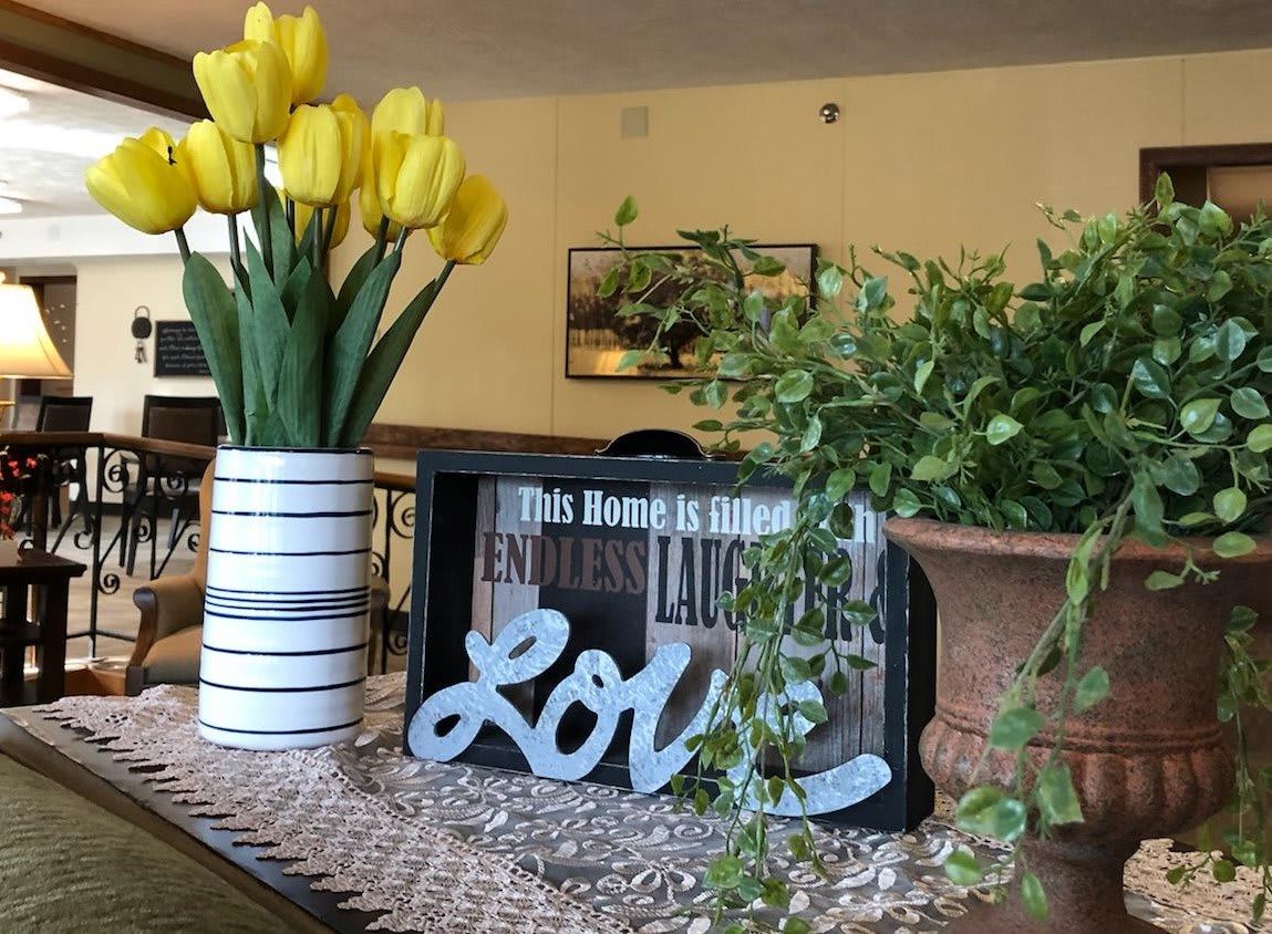 A cozy home decor setup featuring a vase of yellow tulips, a decorative love sign, and greenery.