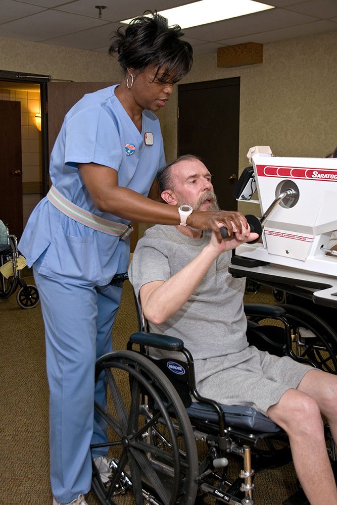 A nurse assists a patient in a wheelchair with using a device.