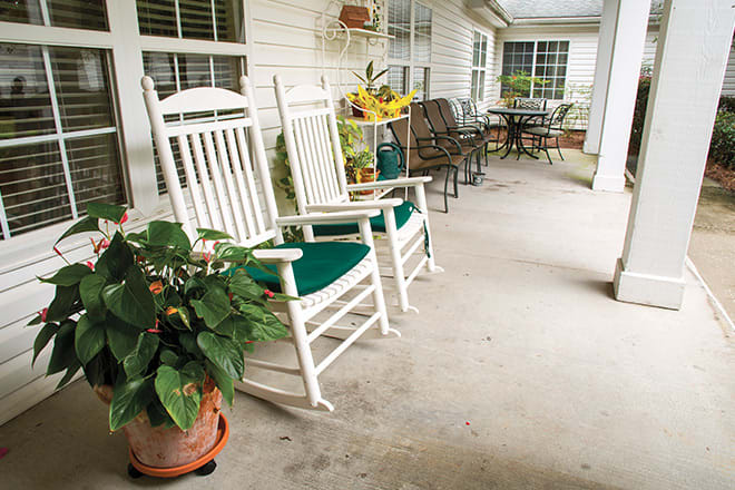 Cozy porch setting with white rocking chairs and potted plants.