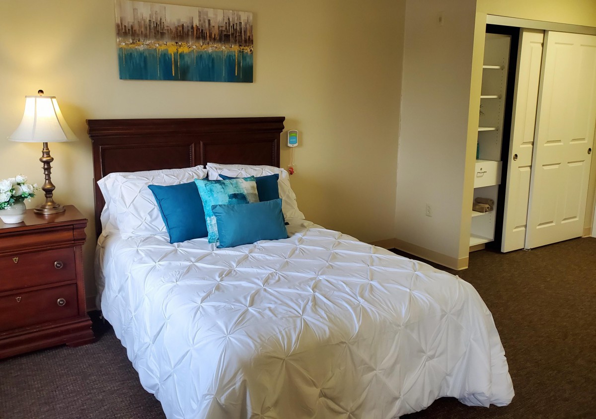 A cozy bedroom with a neatly made bed featuring blue accent pillows and a white comforter, complemented by wall art.