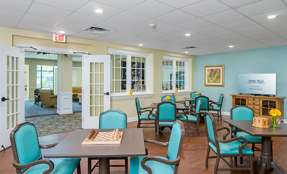 A well-lit dining area with teal chairs and tables, featuring a chess board on one of the tables.