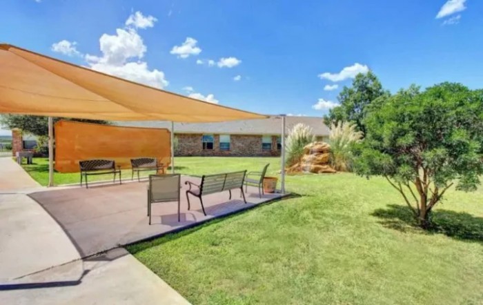 A sunny backyard with a shaded patio and outdoor seating area.