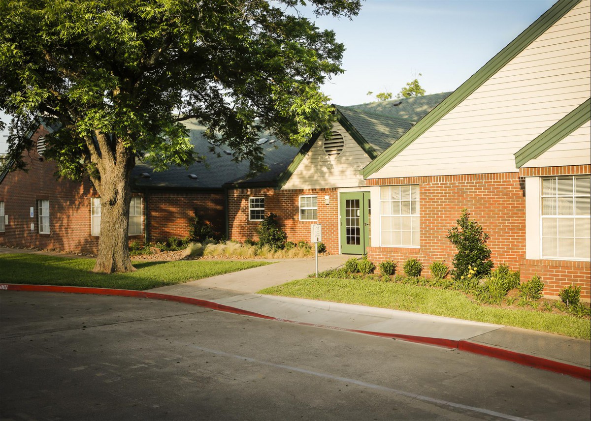 A suburban brick house with a driveway and a tree in the front yard.