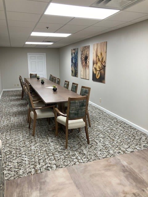 A modern conference room with a long wooden table, surrounded by chairs and adorned with artwork on the walls.