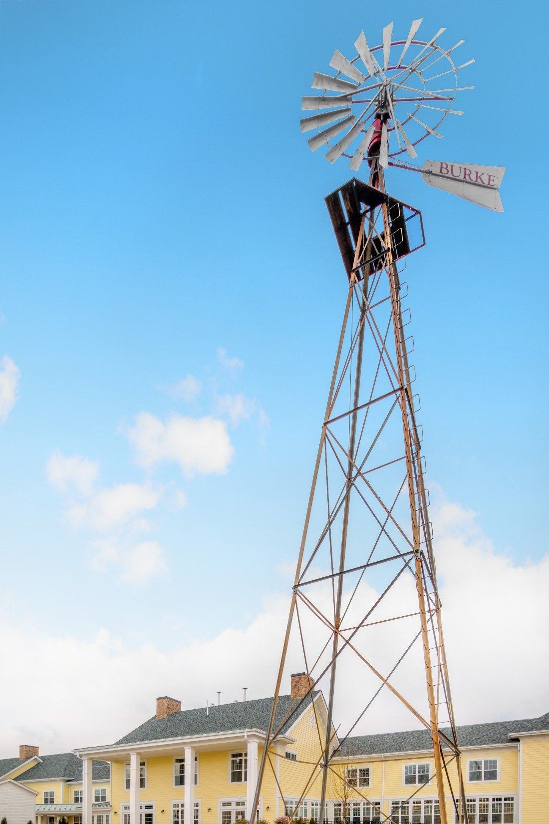 A tall windmill standing against a clear blue sky with scattered clouds.