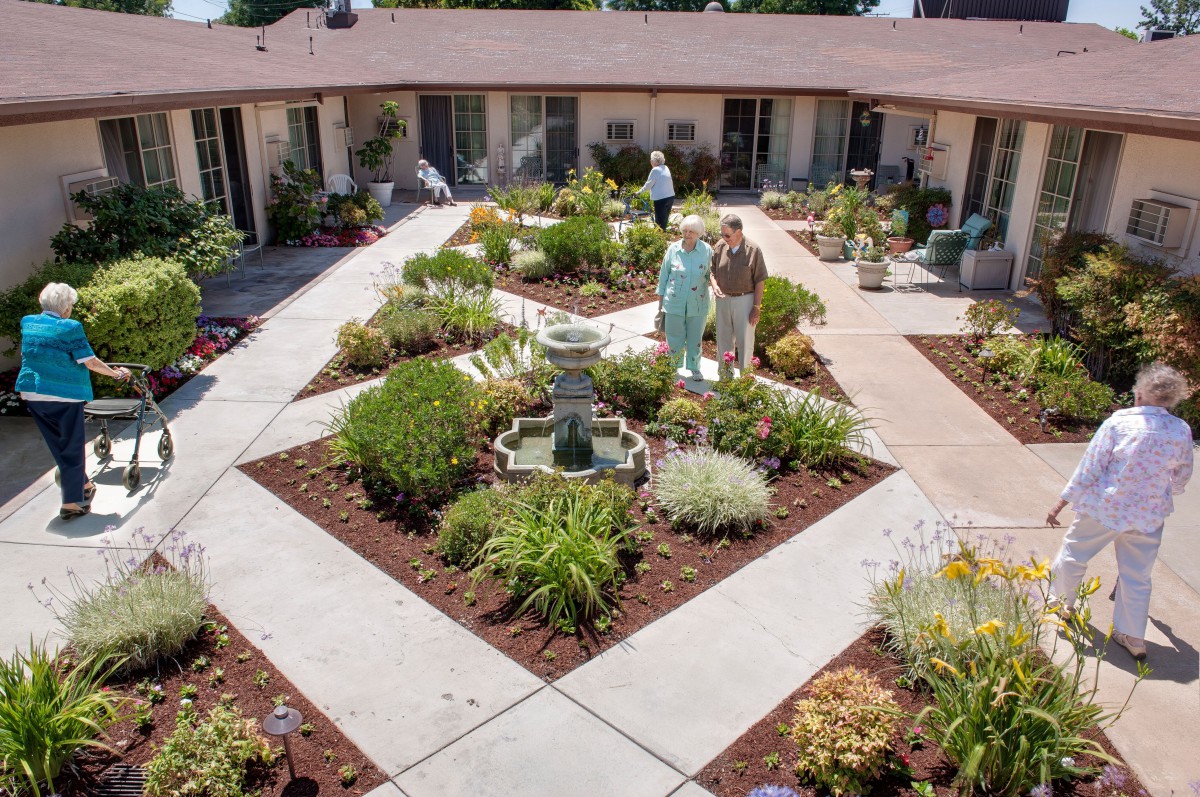 A well-maintained courtyard garden with a central fountain, surrounded by pathways and various plants.
