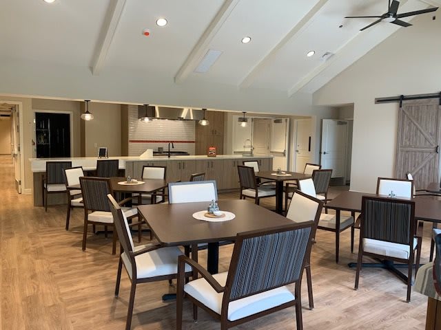 A modern dining area with tables and chairs arranged neatly in front of a kitchen counter.