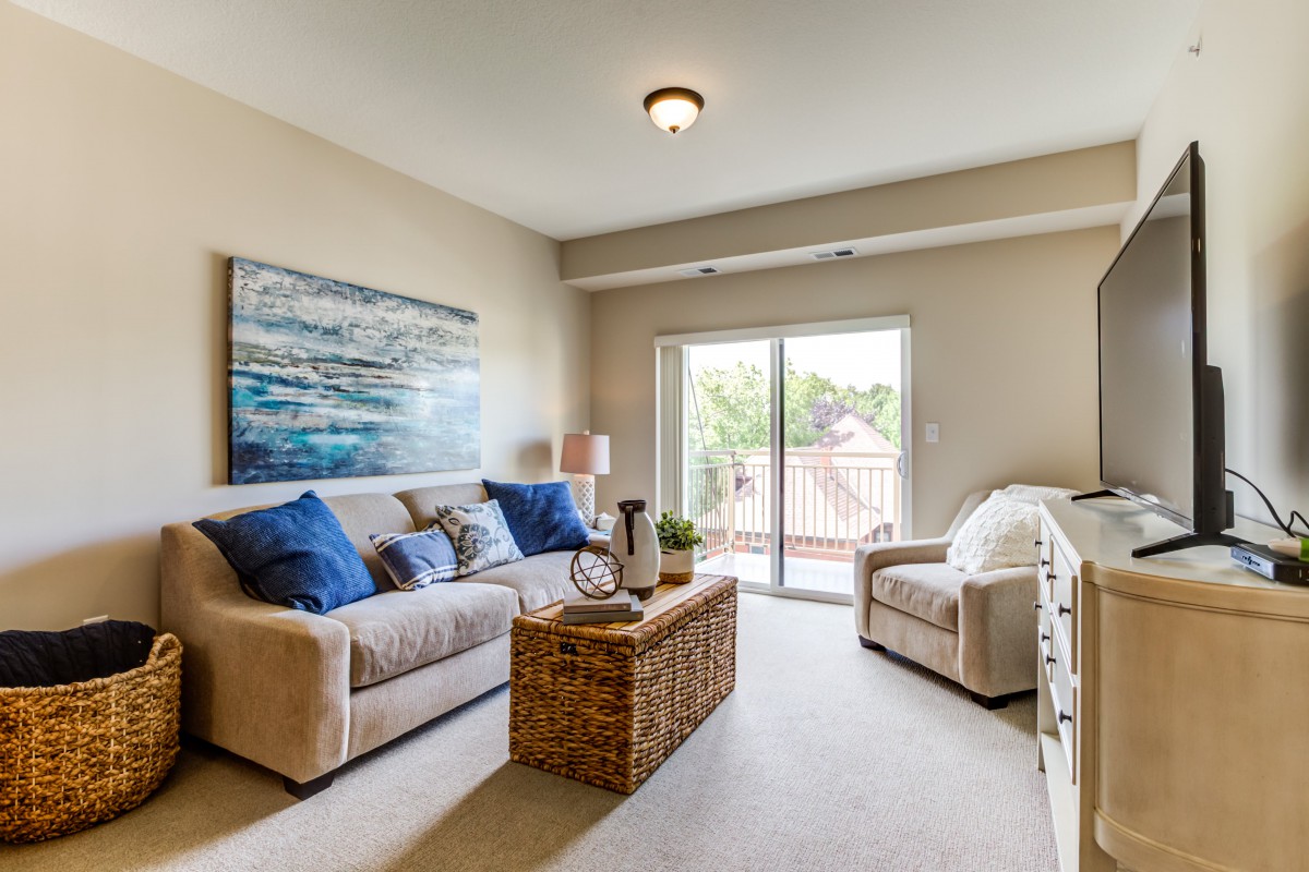 A cozy living room with a sofa, armchair, and coffee table, featuring artwork and abundant natural light through a sliding glass door.