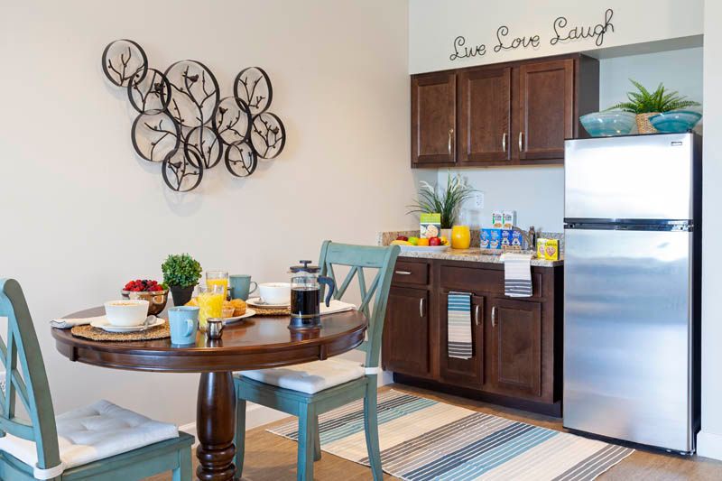 A cozy kitchen and dining area featuring wooden cabinets, a round table with chairs, and decorative elements on the wall.