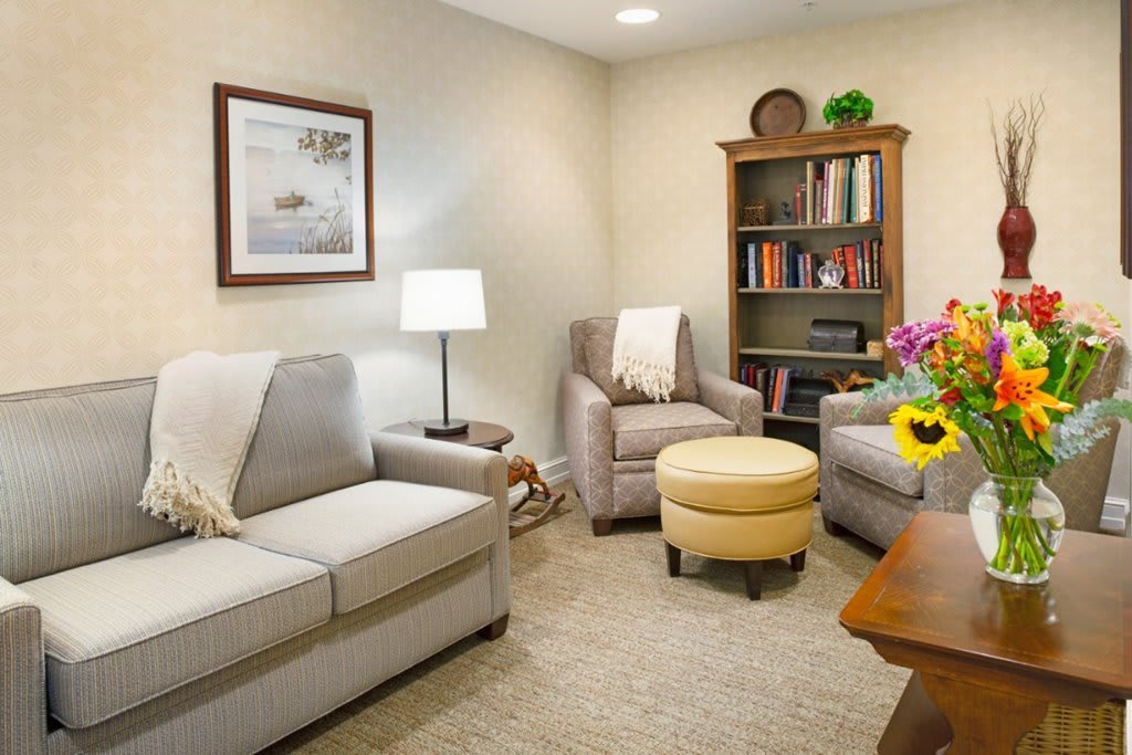 A cozy living room with a sofa, armchair, lamp, and a bookshelf filled with books.