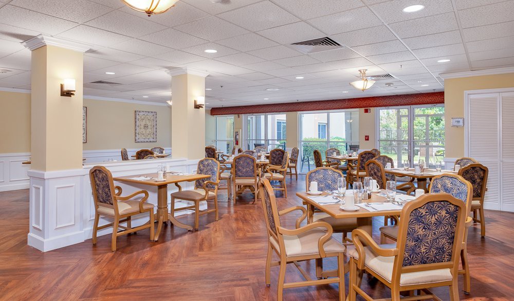 A spacious dining area with wooden tables and chairs, featuring large windows and wooden flooring.